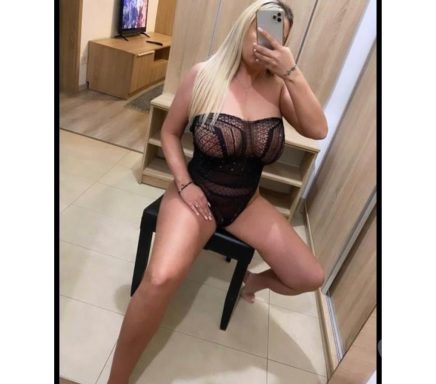 A person sitting on a chair, taking a selfie while wearing a black lingerie outfit.