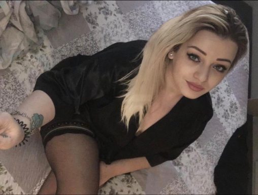 Young woman with long blonde hair wearing a black top and holding a smartphone.