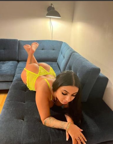 Woman in a yellow outfit lying on a blue sofa, resting on her elbows.