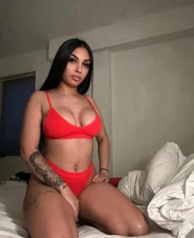 A woman in a red bikini, sitting on a bed among white pillows.