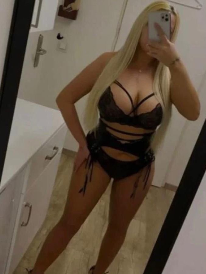 A person posing in a revealing black outfit with cut-out sections.