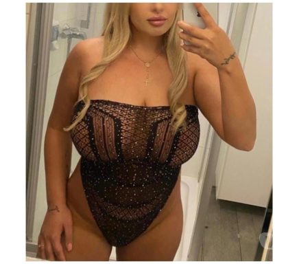 A person in a sheer black bodysuit posing for a mirror selfie.